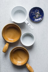 Top view of brown and white ceramic ramekins on a white marble countertop, terracotta ramekins with handles on a white background