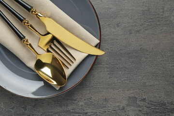 Elegant setting with golden cutlery on dark grey table, top view. Space for text