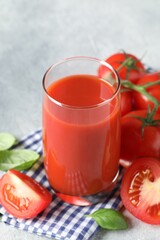 Tasty tomato juice in glass, basil leaves and fresh vegetables on grey table