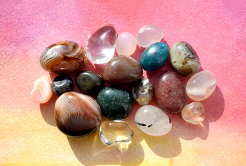 Colorful semi-precious stones illuminated by sunlight lie on a bright pink background. Healing crystals.