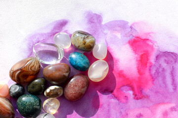 Colorful semi-precious stones illuminated by sunlight lie on a bright pink background. Healing...