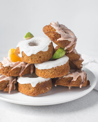 Stack of iced mini bundt cakes with citrus fruit garnish, glazed bundtlette cakes stack on a white ceramic plates, mini cakes with a white and orange icing