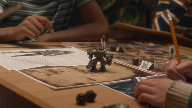 Midsection shot of group of unrecognizable kids playing tabletop game. Making move with action figure and rolling dice indoors