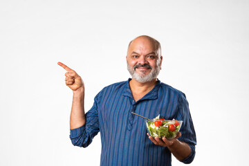 Senior Indian asian man eating fresh salad. Mature male having healthy snack, healthcare, diet...