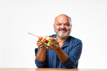Senior Indian asian man eating fresh salad. Mature male having healthy snack, healthcare, diet...