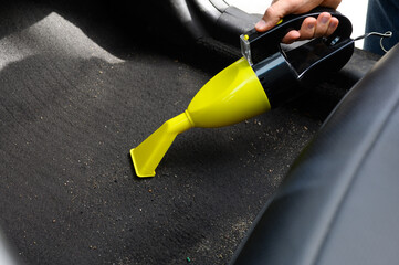 Man cleans floor of car with yellow vacuum cleaner. Heavily soiled car mat is cleaned by car...
