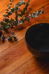 empty dark bowl mock up with a dry eucalyptus branch on wooden board background