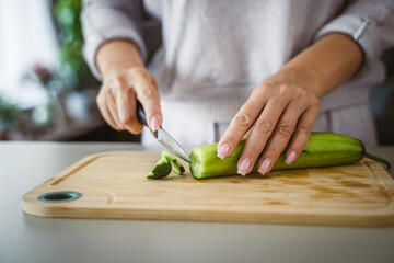 An unknown adult caucasian woman stand and cut cucumber at home