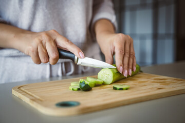 Obraz premium An unknown adult caucasian woman stand and cut cucumber at home