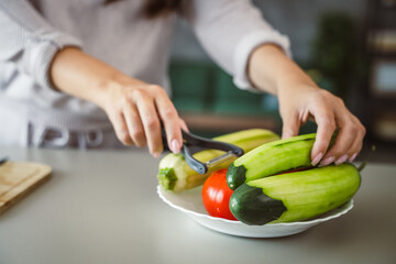 Unknown adult caucasian woman stand and peel a cucumber at home