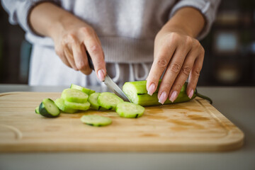 An unknown adult caucasian woman stand and cut cucumber at home