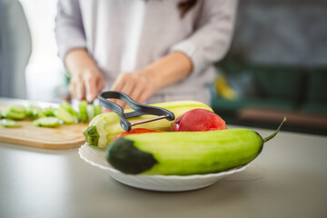 An unknown adult caucasian woman stand and cut cucumber at home