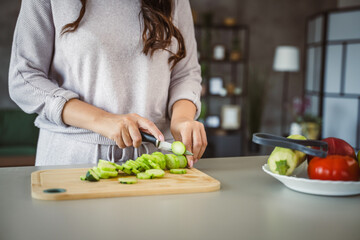 An unknown adult caucasian woman stand and cut cucumber at home