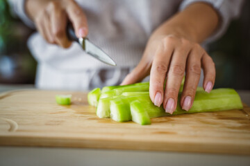 An unknown adult caucasian woman stand and cut cucumber at home
