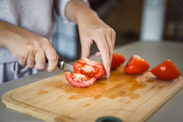 An unknown woman stand and cut tomato with knife on table at home