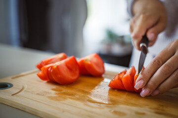 An unknown woman stand and cut tomato with knife on table at home