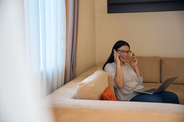 Obraz premium Pleased Asian lady with laptop talking on mobile phone