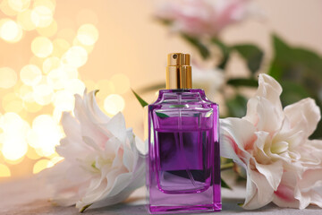 Bottle of perfume and beautiful lily flowers on table against beige background with blurred lights, closeup