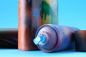 Spray paint cans and caps on light blue background, closeup