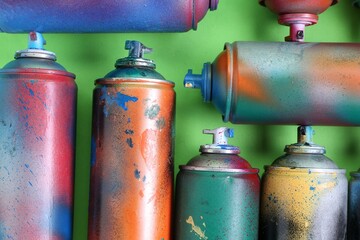 Many spray paint cans on green background, flat lay