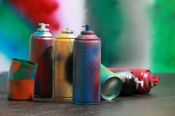 Many spray paint cans on gray surface against color background