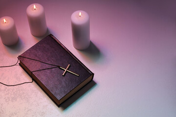Cross, burning candles and Bible on textured table in color lights, above view with space for text....