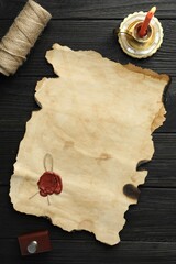 Sheet of old parchment paper with wax stamp, twine and candle on black wooden table, top view