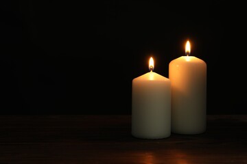 Two burning church candles on black background, space for text