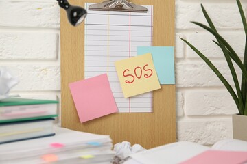 Note with word SOS and stationery on table at workplace