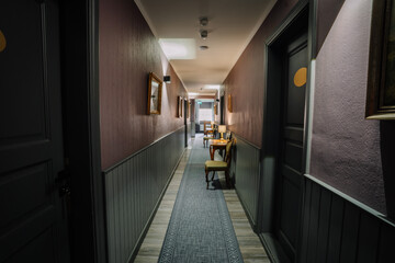 A warmly lit hotel corridor with elegant wooden furniture, framed pictures on the walls, and a patterned rug. A welcoming and serene atmosphere.