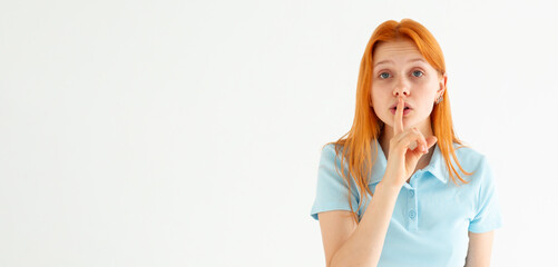 Woman ready to tell secret of beauty. Portrait of charming flirty caucasian female making shush or shh gesture with index finger over mouth, looking sensually and confident at camera over white wall