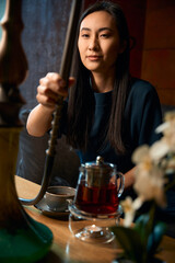 Excited Asian woman holding smoking pipe, enjoying scented hookah