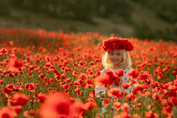 A young girl is standing in a field of red poppies. She is wearing a red headband and a white...