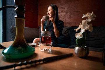 Positive Asian woman sincerely laughing holding cup of warm tea
