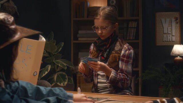 Medium shot of Caucasian cowgirl in glasses choosing card during role playing game, her diverse friends watching her at home in evening