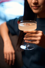 Asian woman looking at goblet with tasty sweet cocktail