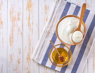 Greek yogurt or sour cream in a wooden bowl and jar of honey on light table, top view.