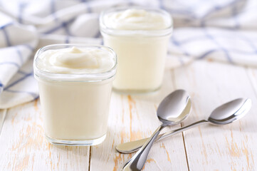 Homemade greek yogurt in a glass jars with spoons on a rustic table, selective focus.