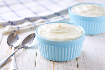 Natural yogurt in a ceramic bowl with spoon on a light background, selective focus.