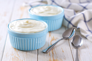 Greek yogurt in a ceramic bowl with spoon on a white table, selective focus.