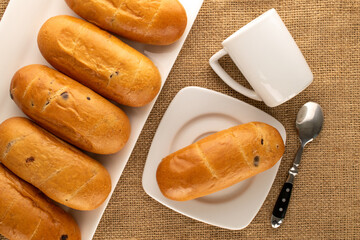 Several sweet buns with ceramic saucer and cup on jute cloth, macro, top view.