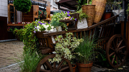 a quaint urban alleyway enhanced with rustic wooden carts overflowing with an array of vibrant flowers and plants, creating a charming and green atmosphere.