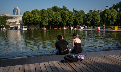People relax near a pond in city park in in the hot summer.