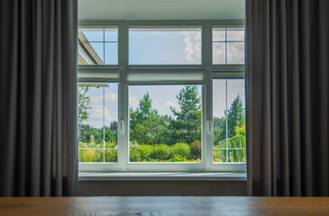 a serene view from a window framed by elegant curtains, looking out onto a vibrant scene of lush greenery, tall pine trees, and a clear sky, offering a tranquil glimpse into the peaceful outdoors.