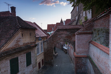 The old stone buildings with tiled roofs, arch and paved road down the street in the early morning in Sibiu, Romania