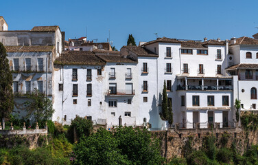 Whitewashed buildings cling to the edge of a steep cliff, their facades a stark contrast to the ruggedness of the precipice, under the vast expanse of a clear blue sky