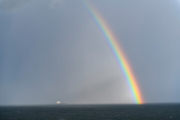 Rainbow at sea. Cargo vessel. Seascape, blue sea.
