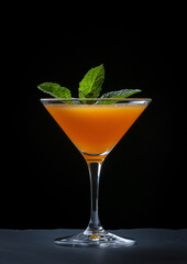 Orange juice in a glass with mint leaves on a black background
