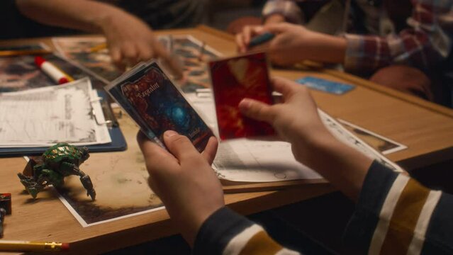 Closeup of hands of anonymous child viewing cards with characteristics during role playing game with friends at table at home