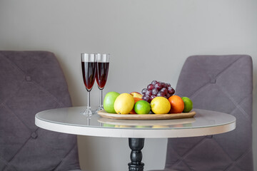 fruits on a wooden plate and two glasses of red wine. Ripe apples, grapes, tangerines and pears on the table.